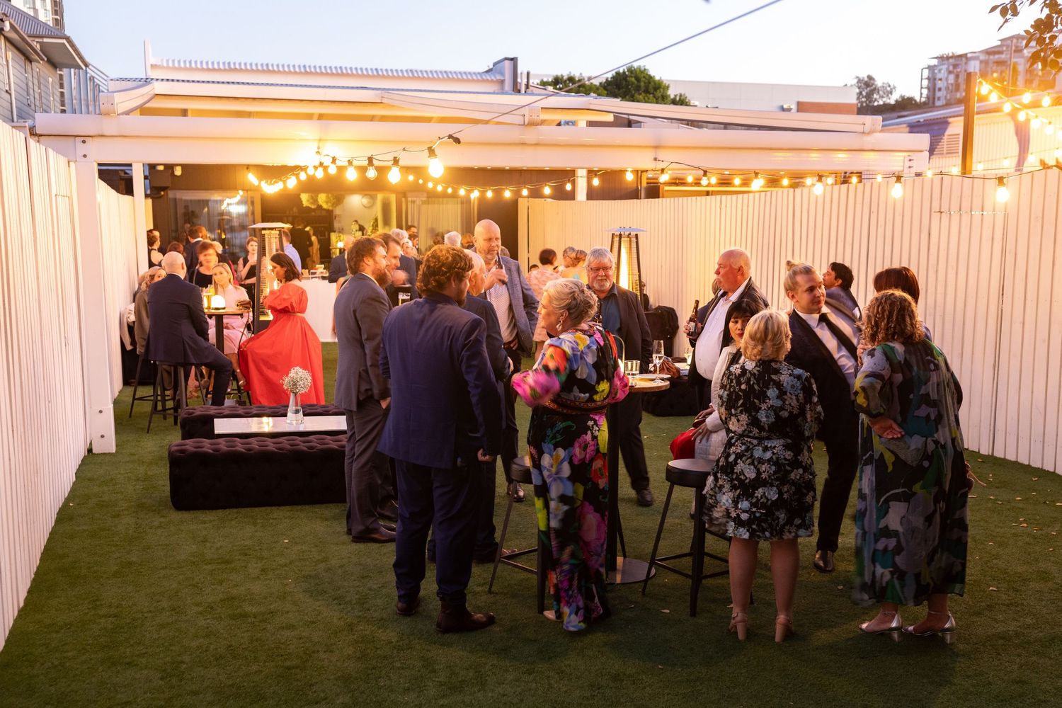 Panoramic view of outdoor wedding reception with white tent and string lights at dusk.