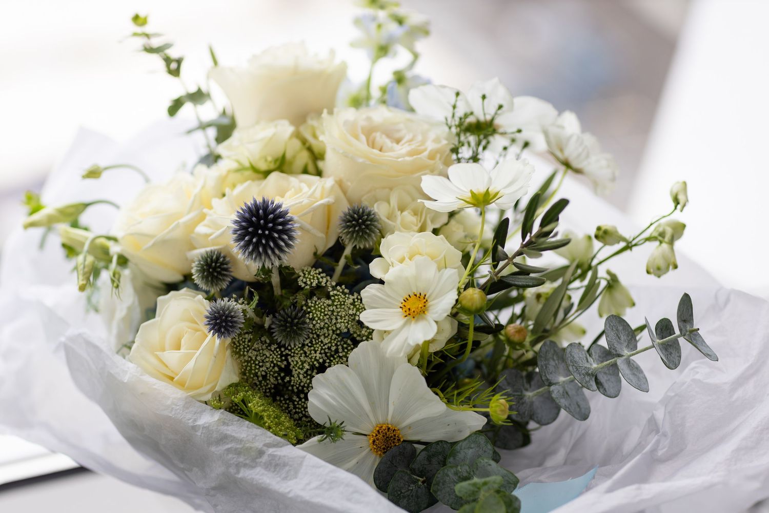 Elegant white floral arrangement with roses, daisies and eucalyptus in soft natural light.