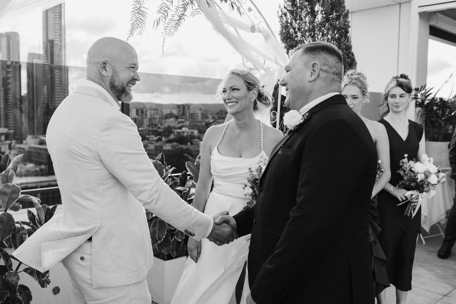 Guests mingle during a wedding reception on a bright outdoor terrace with white decorative elements.