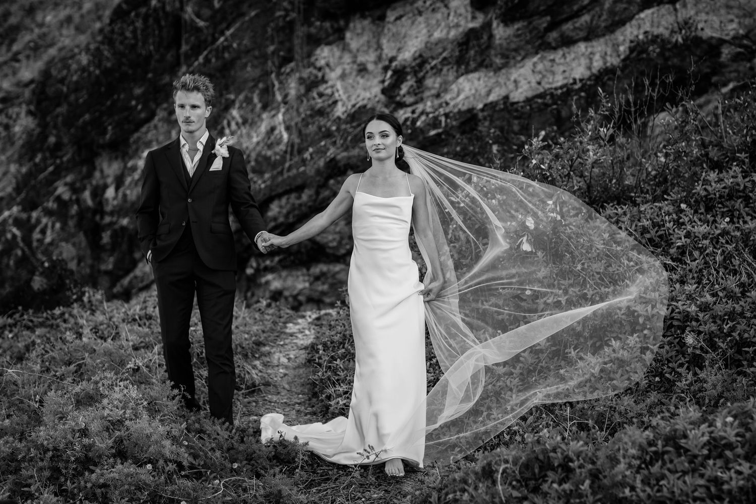 Wedding couple walks along dramatic mountain path with flowing dress.