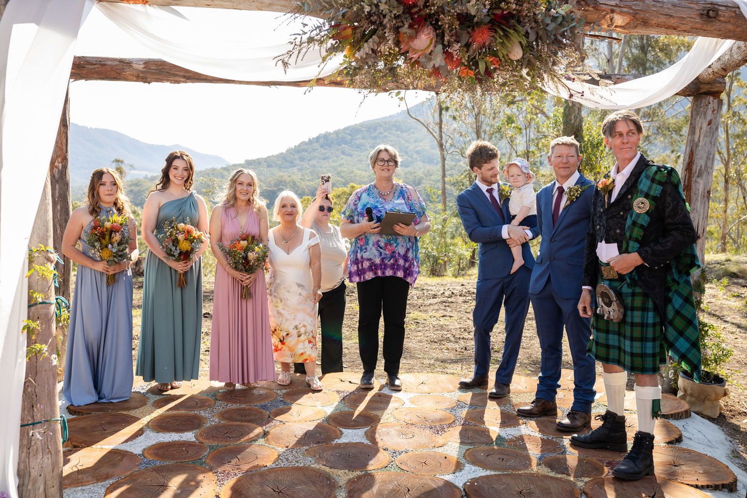 Wedding party arranged under rustic wooden arch decorated with flowers and white fabric.Gold Coast wedding photographer