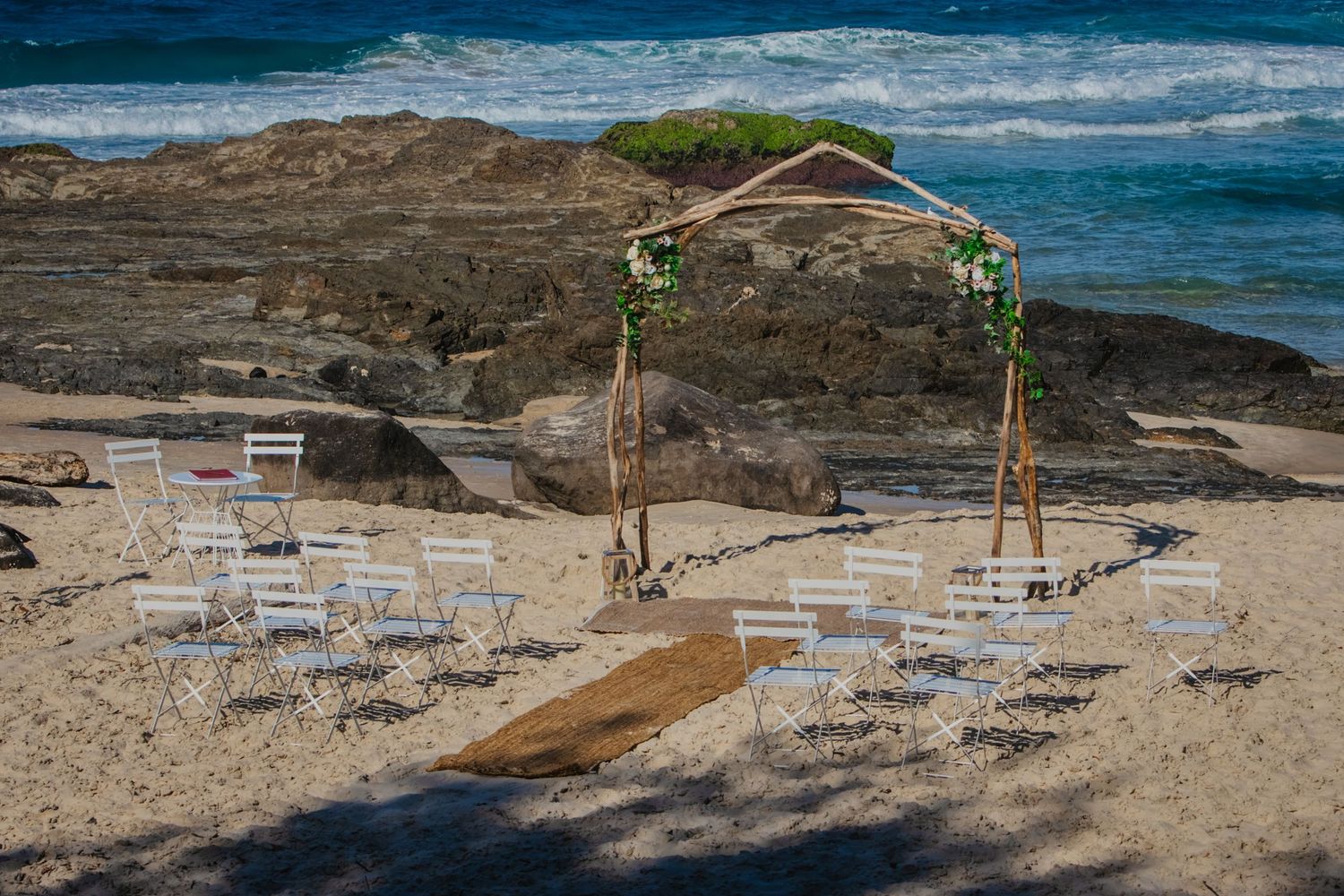 Beach wedding ceremony setup with chairs and archway overlooking rocky coastal waters.