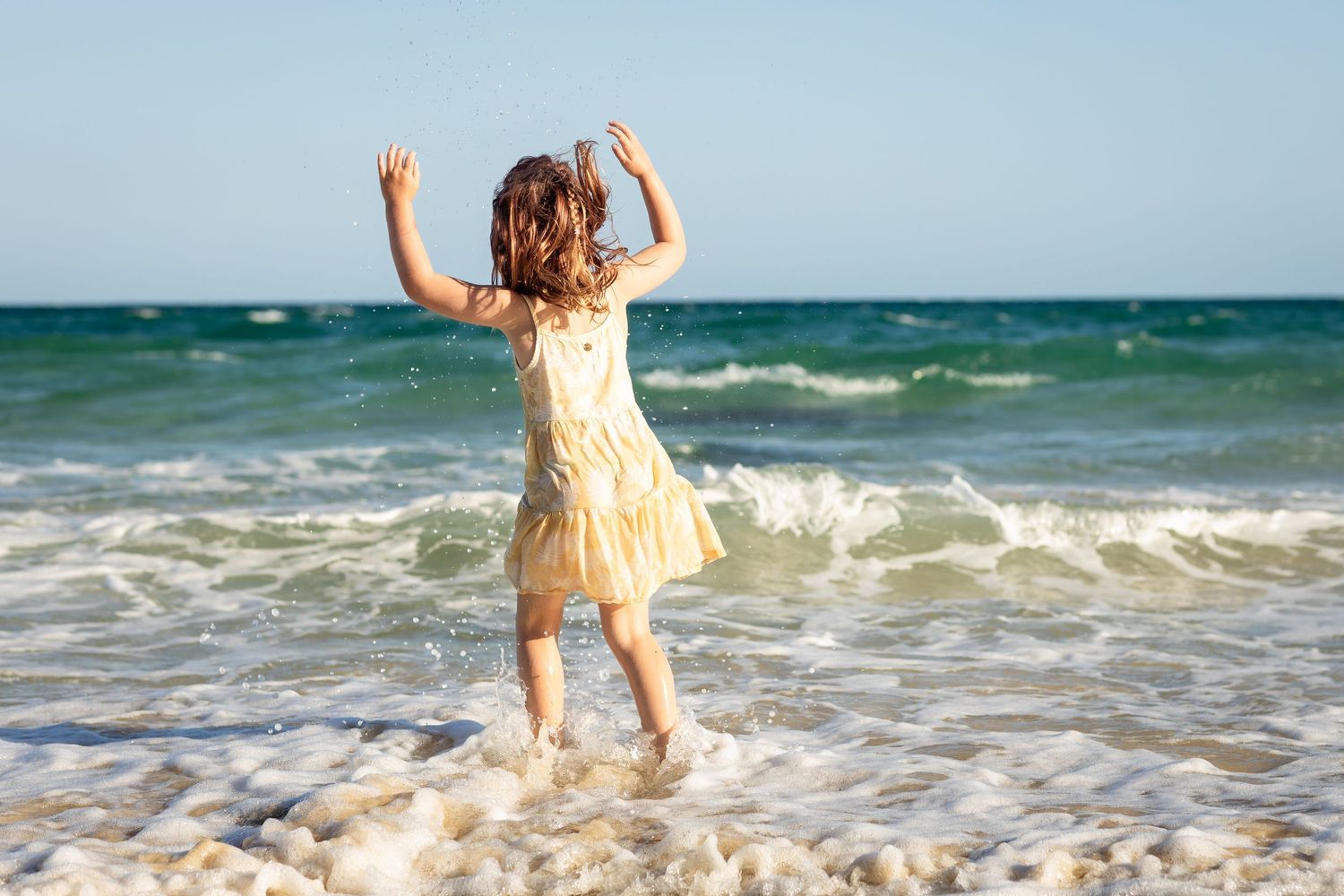 Someone in a light dress splashing in ocean waves on a bright sunny day.Gold Coast candid family photographer.