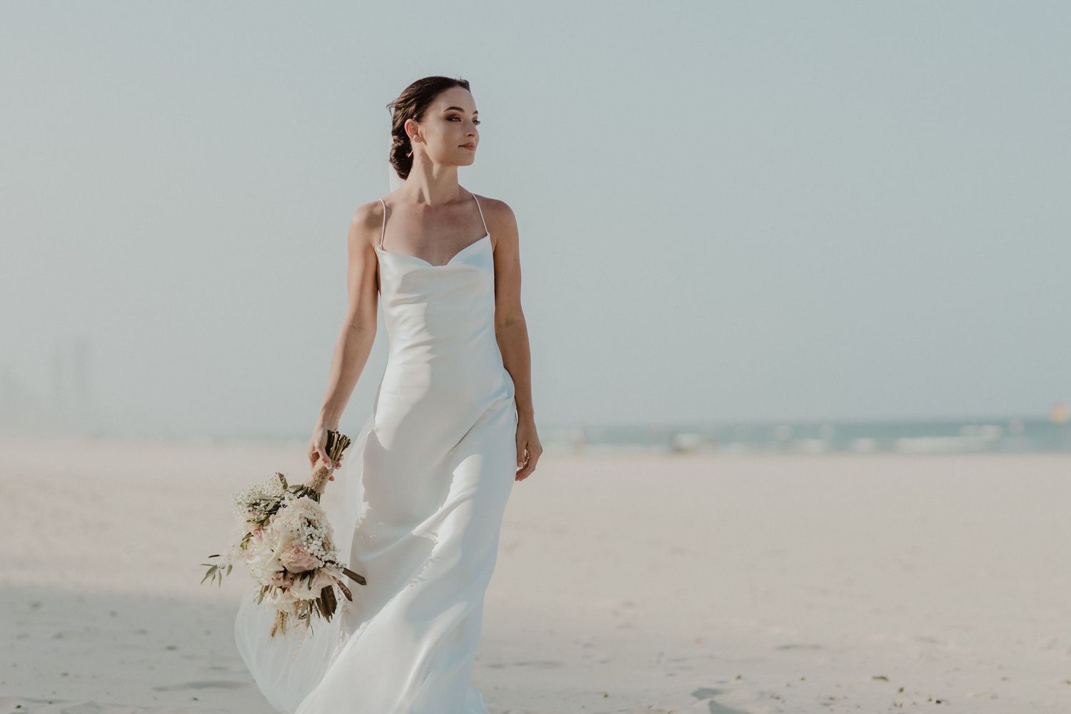 Elegant beach wedding scene with couple walking along the shoreline in formal attire.
