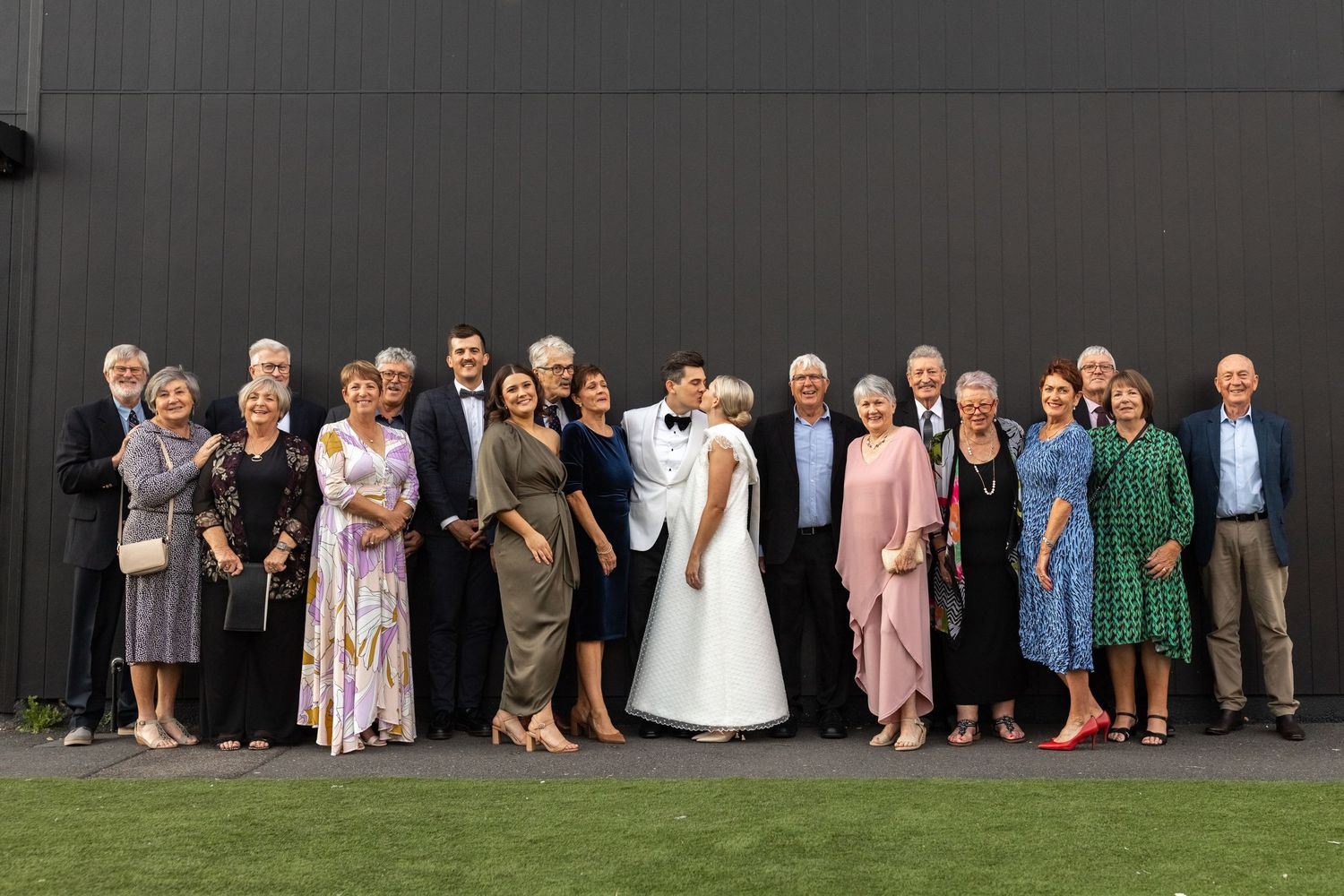 Large wedding party group photo with bridesmaids and groomsmen lined up outdoors.