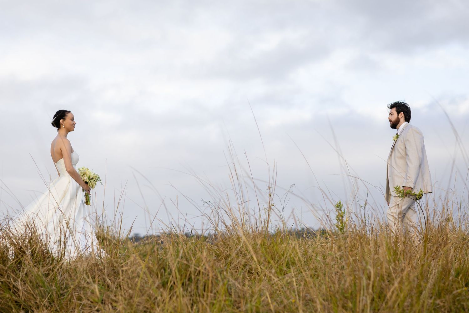 Wedding couple walking through meadow grass against cloudy sky backdrop.The barrow restaurant mount Nathan wedding