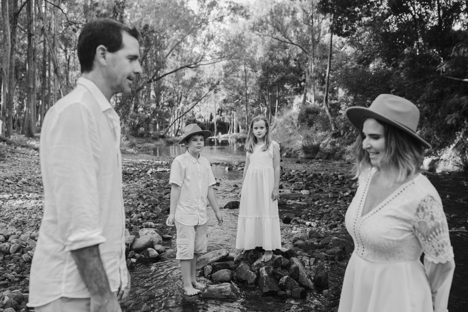 Group in white clothing stands together in a wooded outdoor setting.