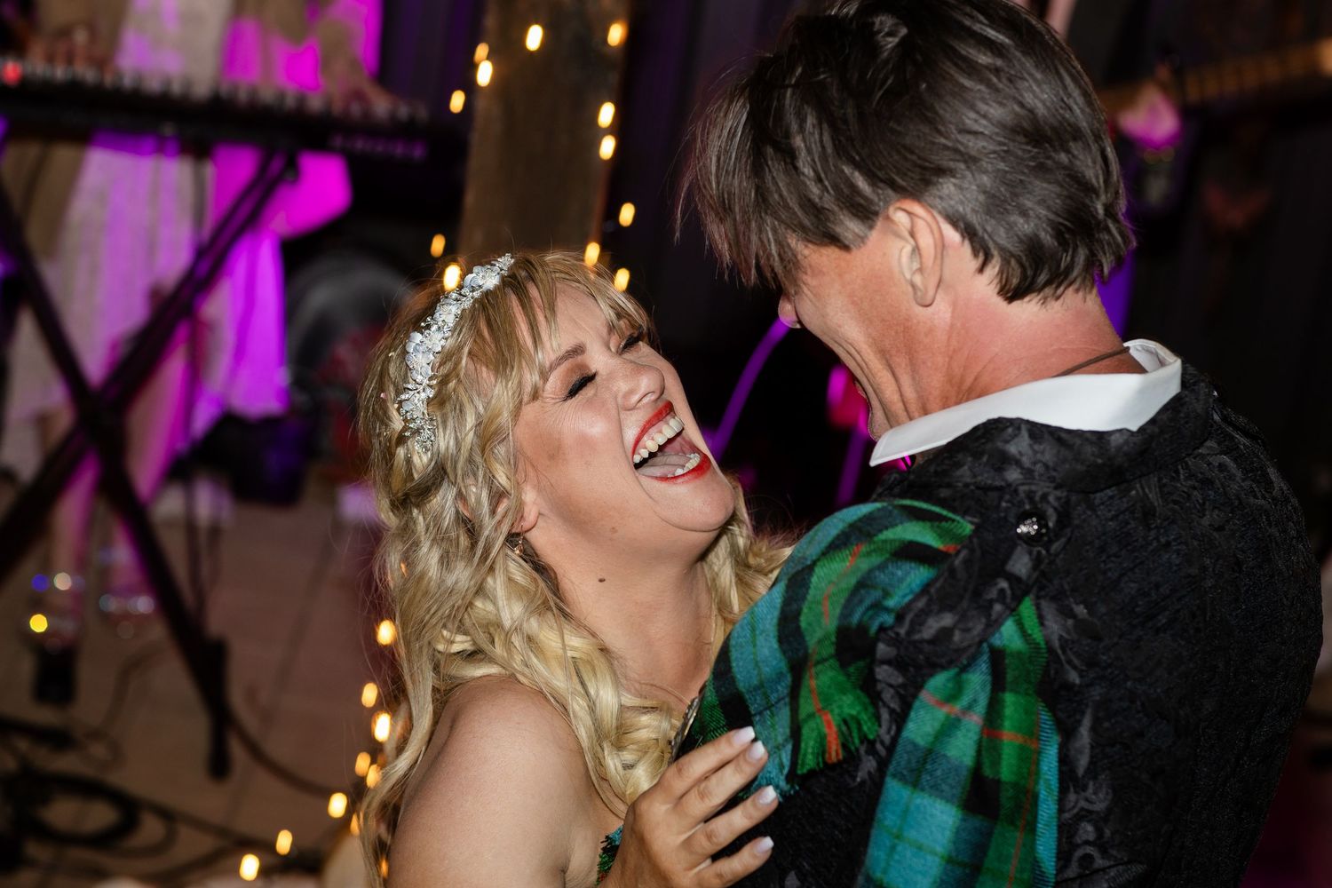 Wedding reception dance floor illuminated with purple lighting and string lights.