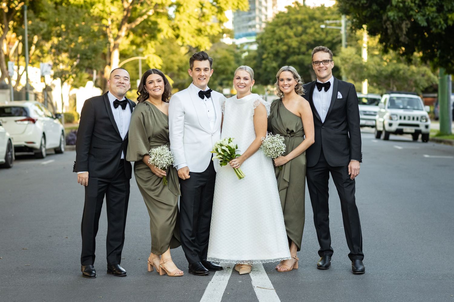 Wedding party walking down sunny street in formal attire.