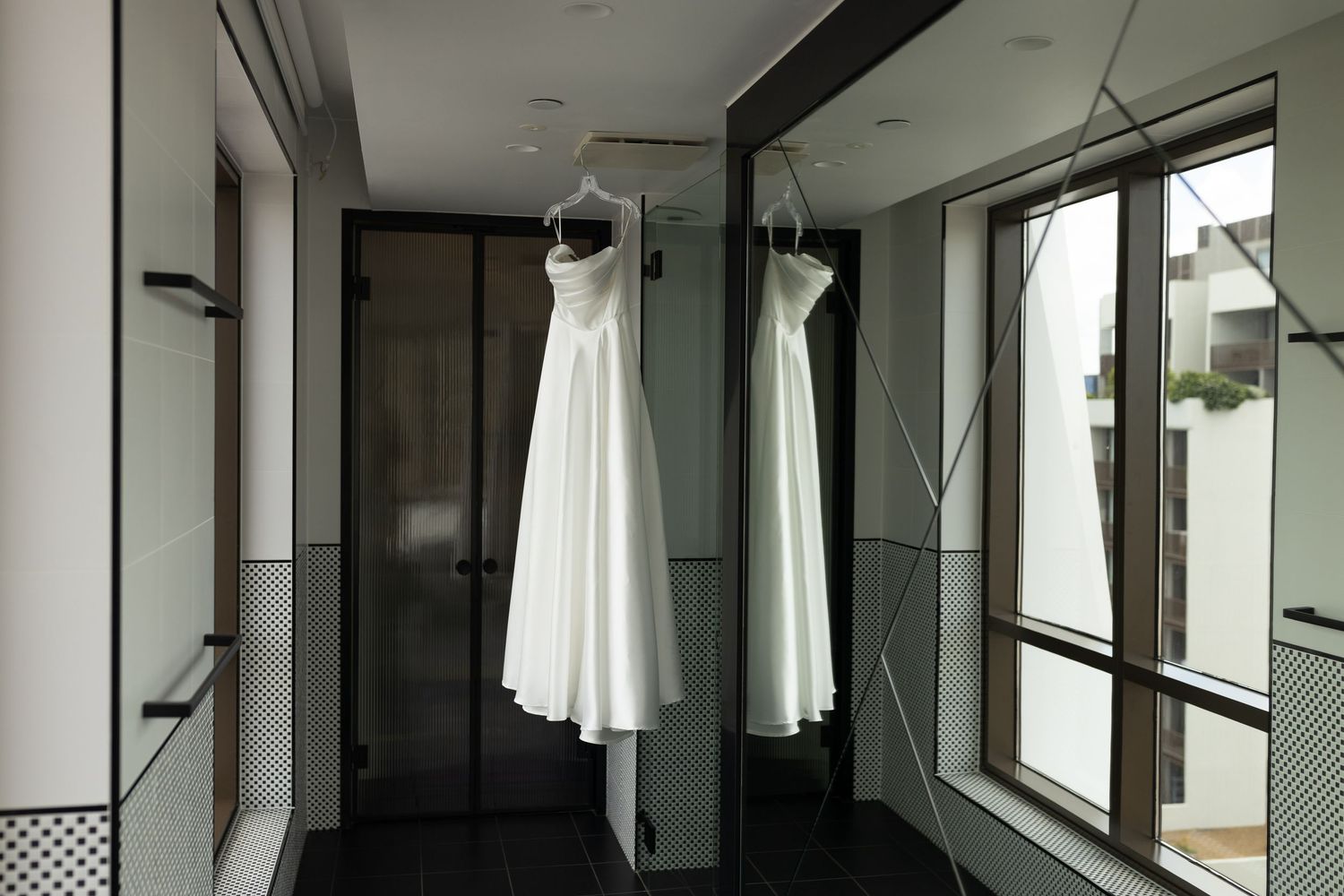 White wedding dress hanging in modern hallway with mirror reflections and natural light.