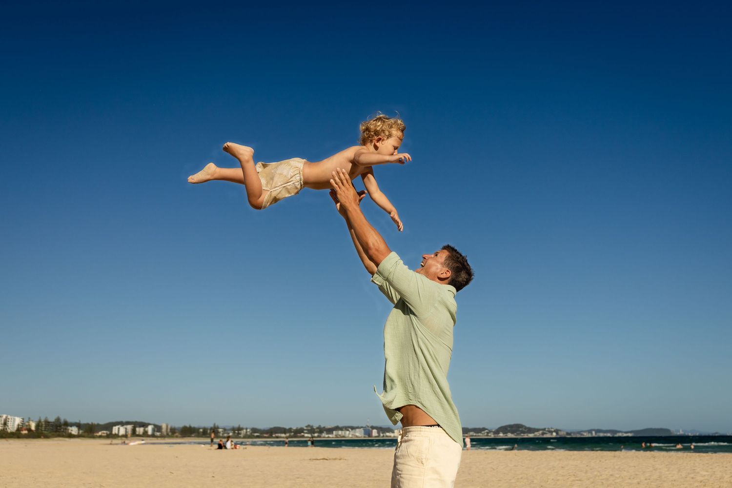 People enjoying activities on a sandy beach with clear blue skies. Family photography Kirra beach Gold Coast.Gold Coast candid family photog