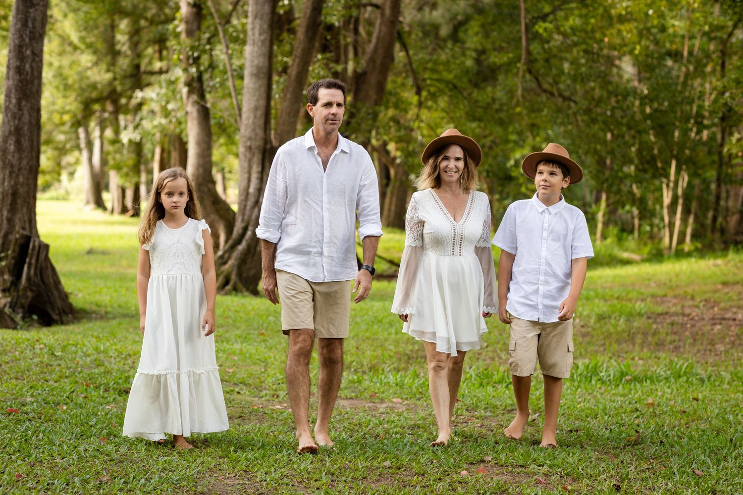 Family walking together through a sunlit grassy park in white summer outfits.Tallebudgera family photography. Gold Coast
