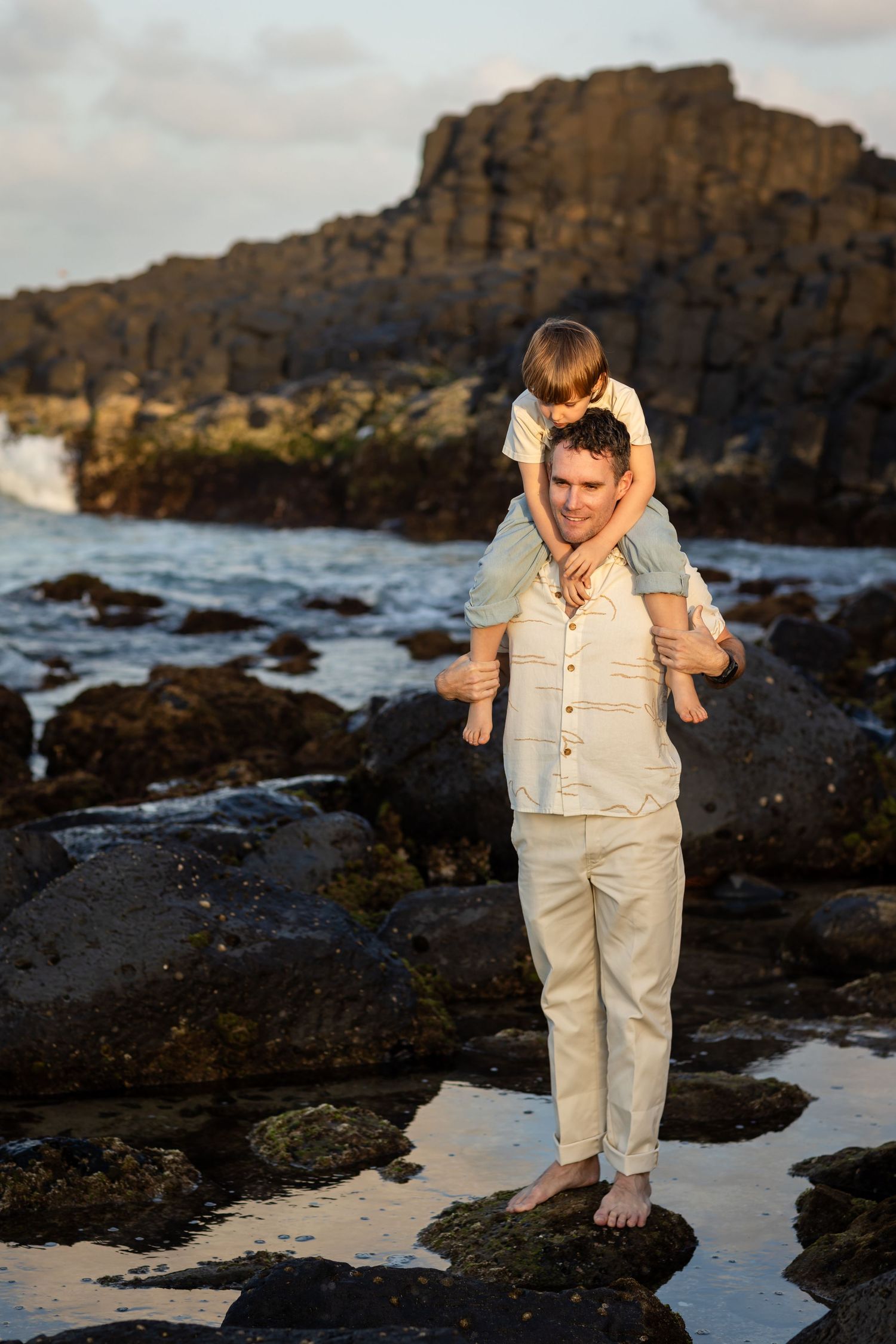 Person in light colored outfit explores rocky tide pools at sunset near ocean cliffs.Fingal head family photos -  New South Wales