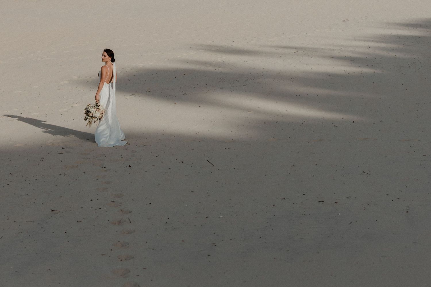 Wedding couple walks along a sandy beach with soft shadows cast on the ground.Miami Burleigh heads beach wedding