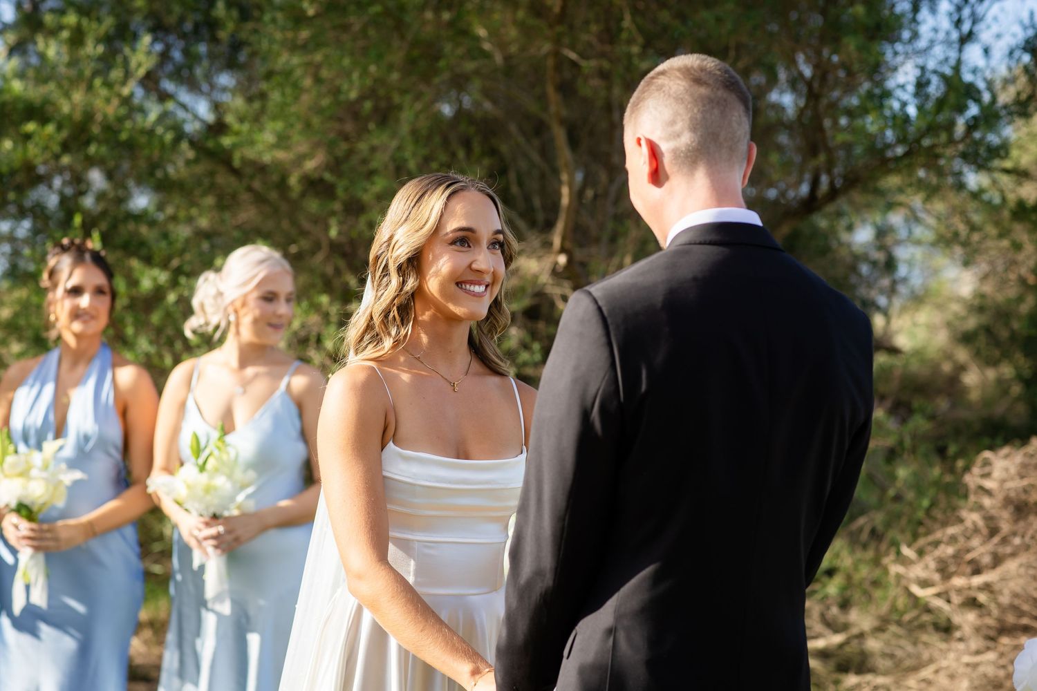 Wedding party in light blue bridesmaid dresses and black tuxedos gathered outdoors.beach wedding currumbin surf club wedding