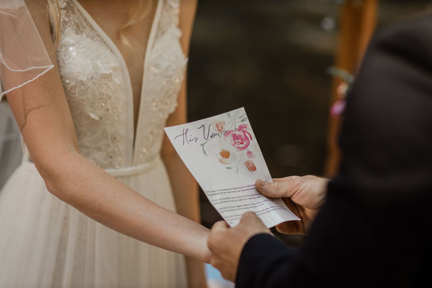 Close-up of hands holding a floral-decorated wedding vow card during ceremony.Currumbin Valley wedding photography Gold Coast