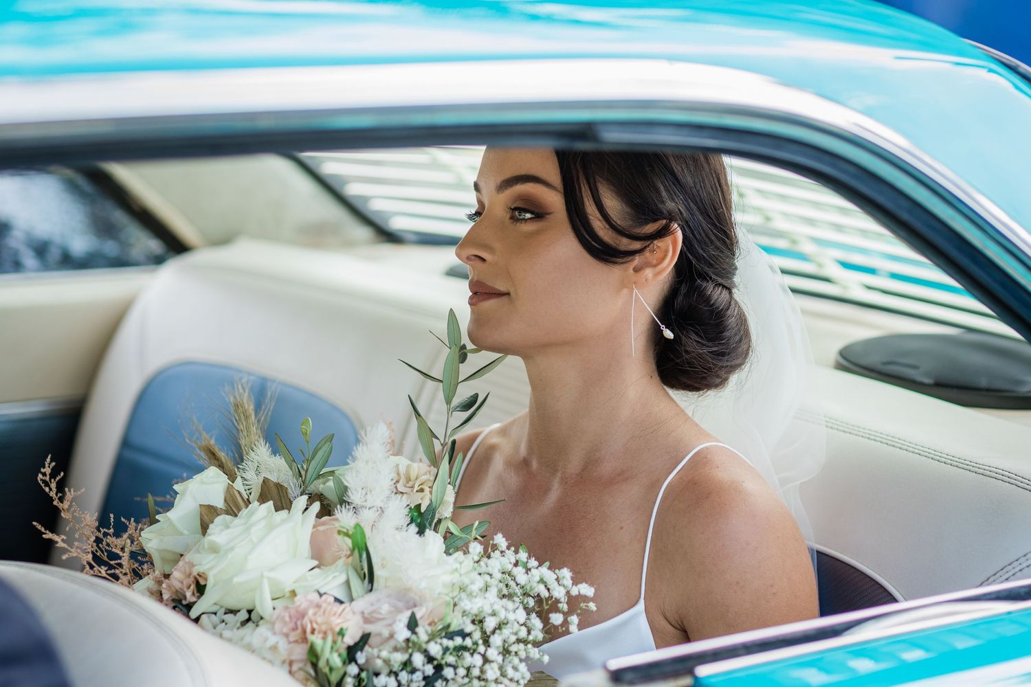 Elegant wedding transportation featuring classic turquoise car and bridal bouquet.