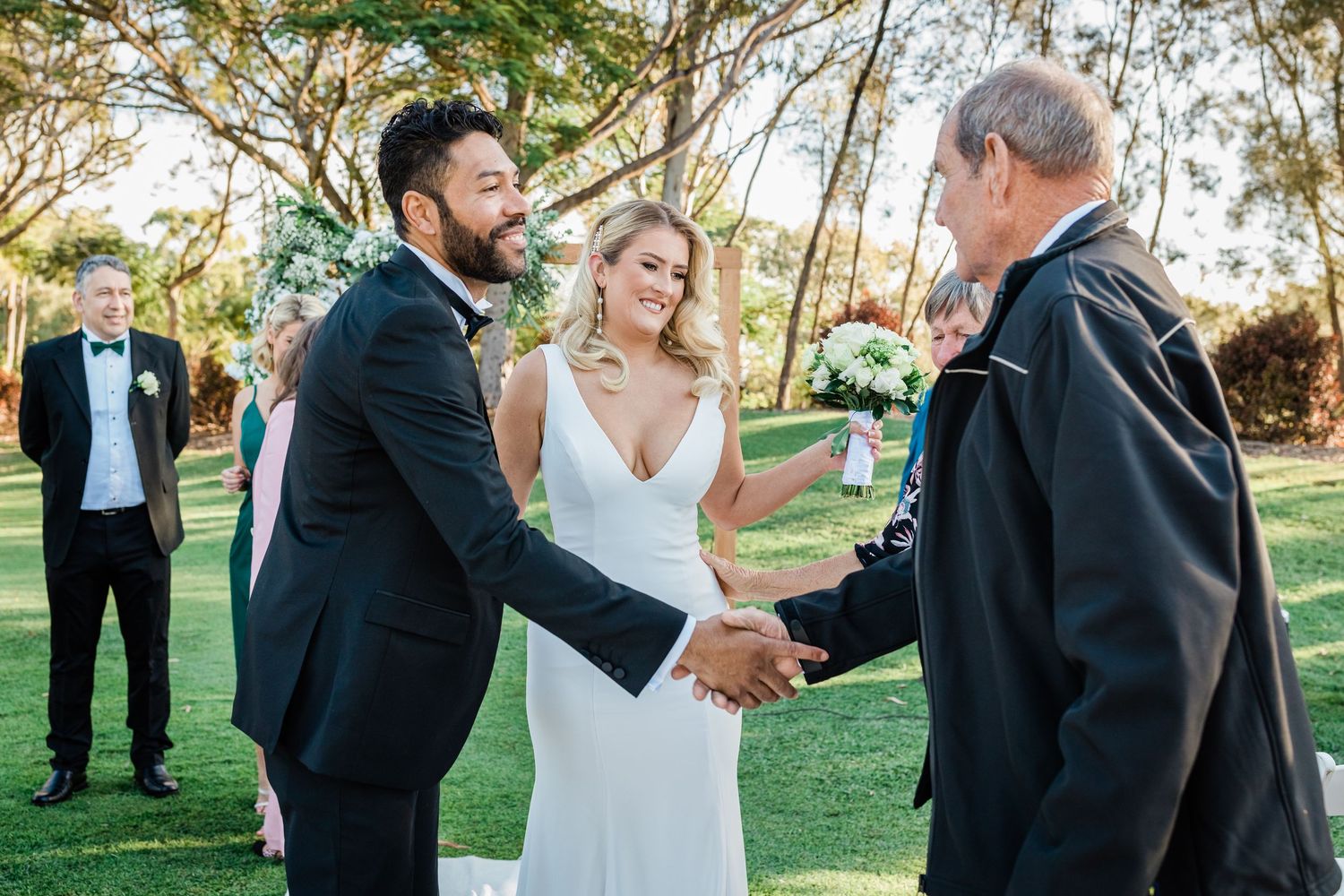 Wedding party members interact and celebrate during an outdoor garden ceremony.