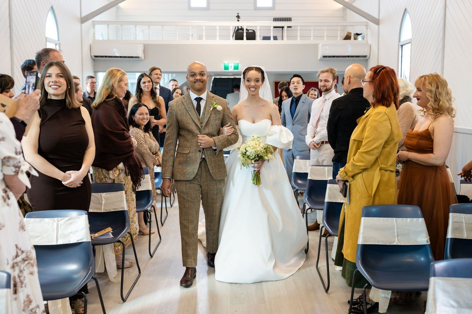 Wedding guests seated in rows of blue chairs inside a modern church venue.Gold Coast hinterland wedding photographer