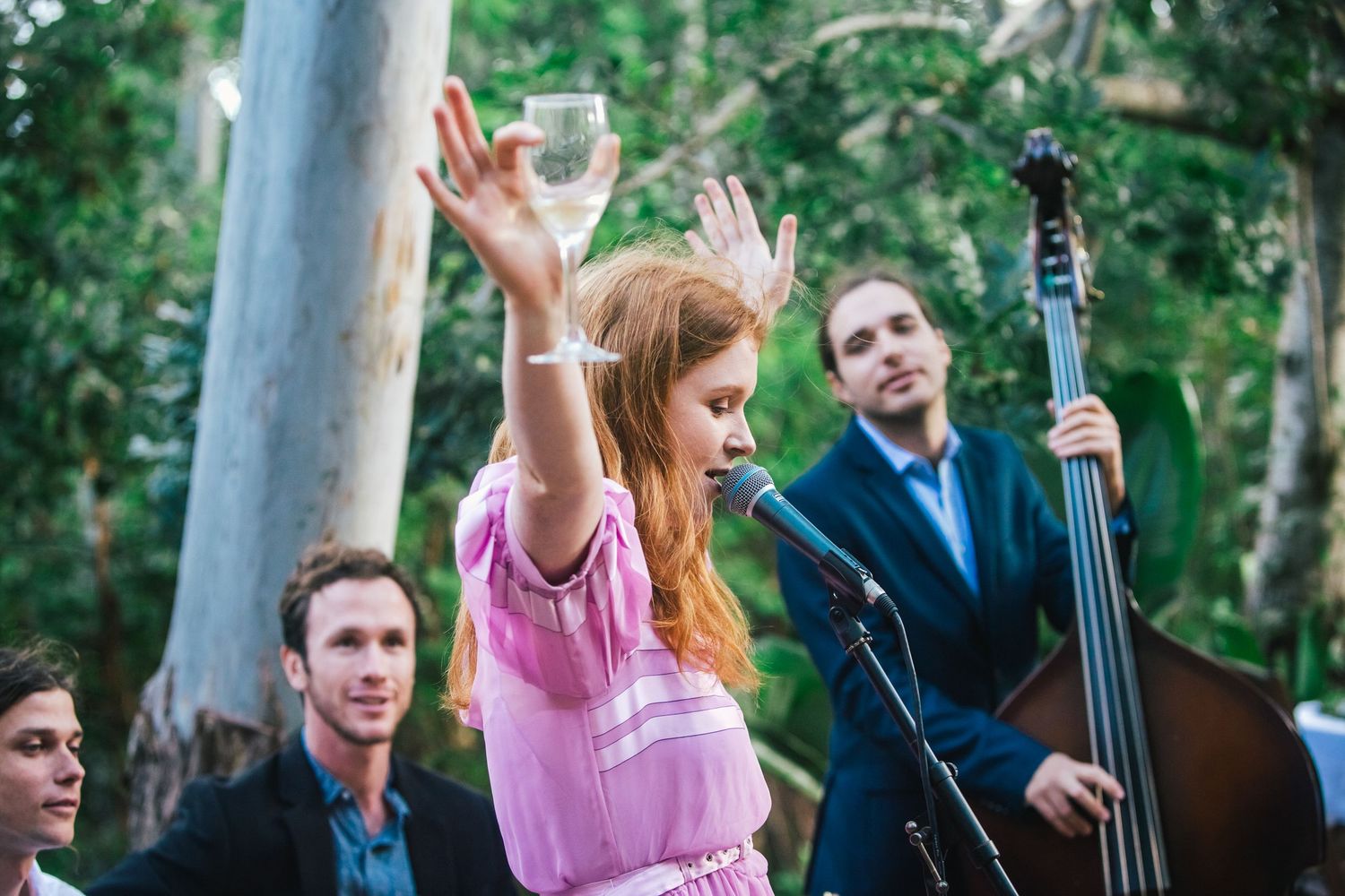 Musicians performing at an outdoor event with string instruments and pink decor.