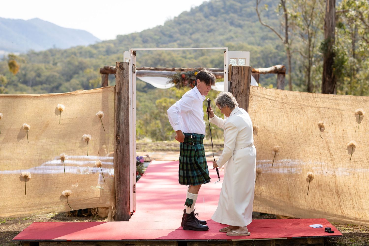 Red carpet aisle runner leading to a rustic wooden wedding arch in a mountain setting.