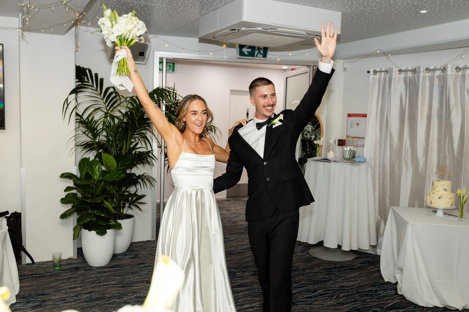 Newlyweds celebrate with raised arms during wedding reception.beach wedding currumbin surf club wedding