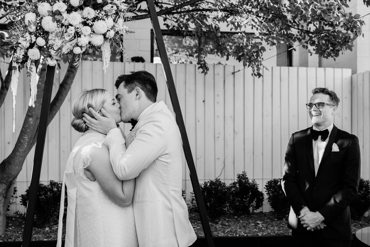 Wedding ceremony taking place outdoors with white fence backdrop.The refinery wedding venue. Brisbane.