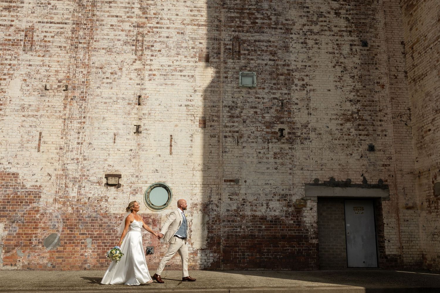 Wedding couple poses against rustic brick wall backdrop in natural light. New farm park wedding photos in Brisbane