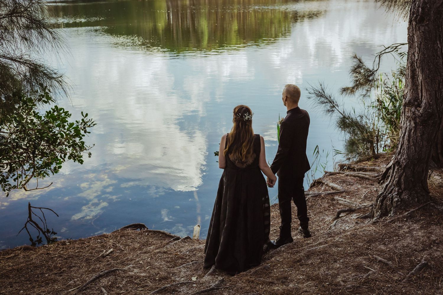People sitting at the edge of a tranquil lake surrounded by trees and reflective water.