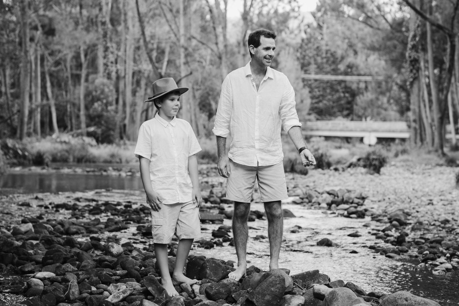 Black and white photograph of people walking along a wooded waterfront path.Tallebudgera family photography. Gold Coast