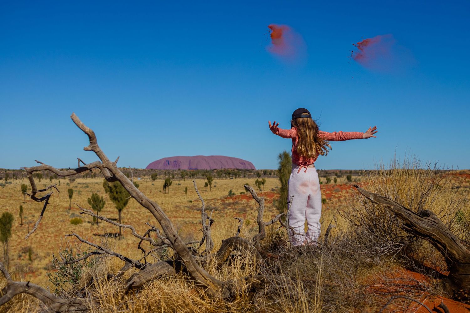 Person in white dress poses dramatically against red desert landscape.