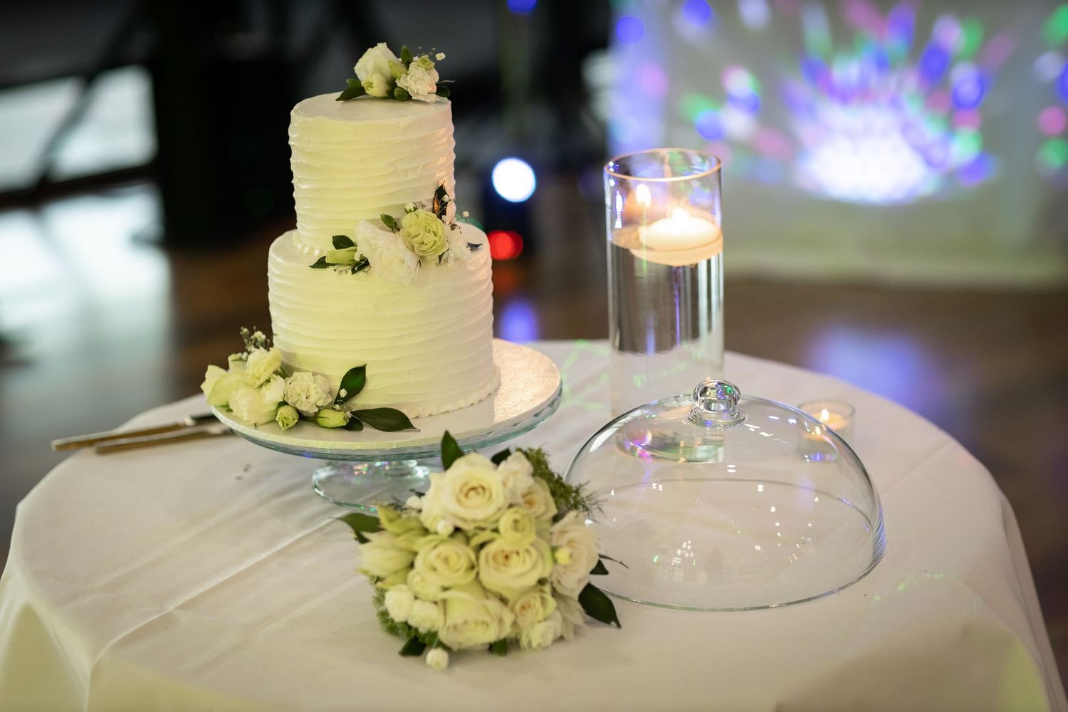 Elegant white wedding cake decorated with fresh flowers on display at reception.
