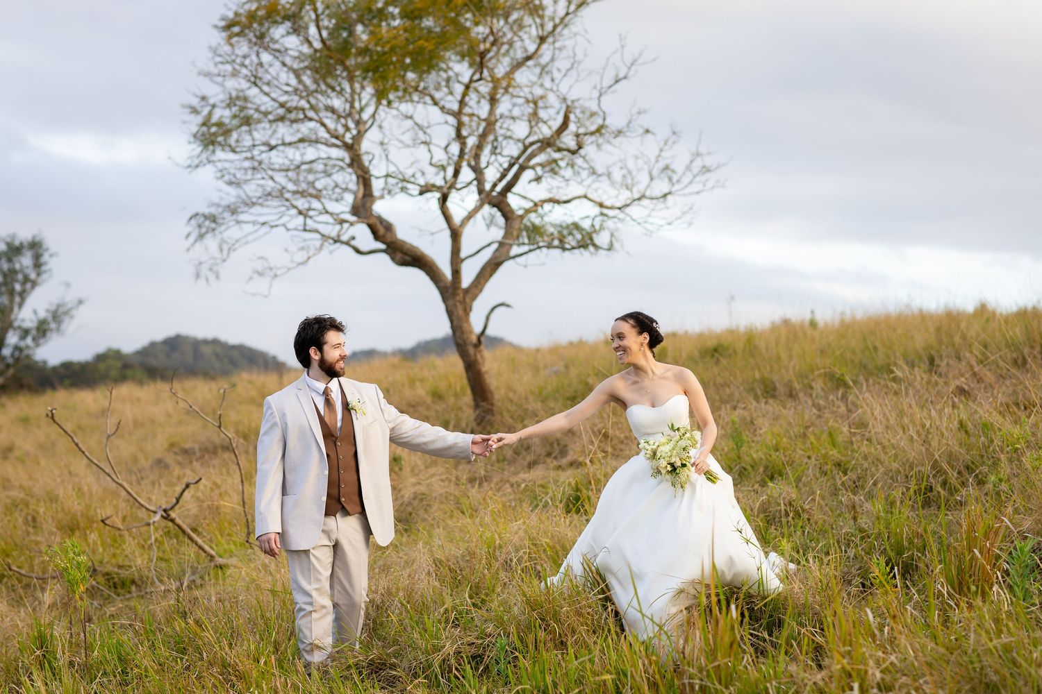 Newlyweds pose together in a rustic field setting with a lone tree in the background.The barrow restaurant mount Nathan wedding