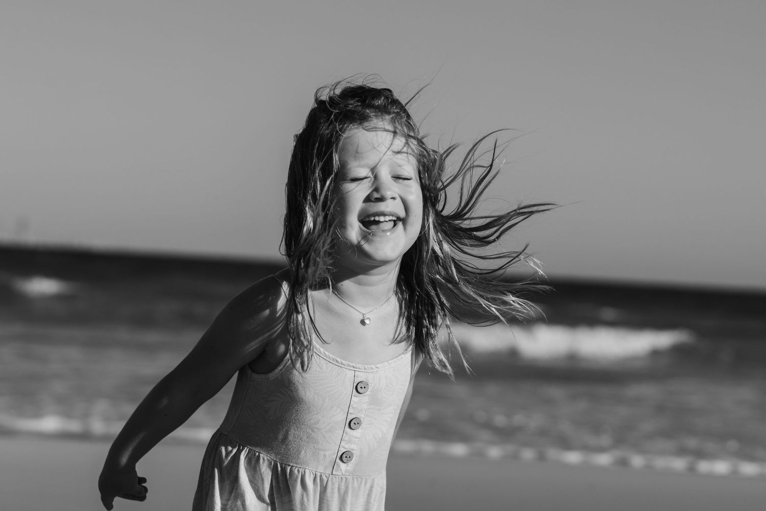 Wind-swept hair and laughter captured in black and white on a beach.Family photography Kirra beach Gold Coast. Gold Coast candid family phot