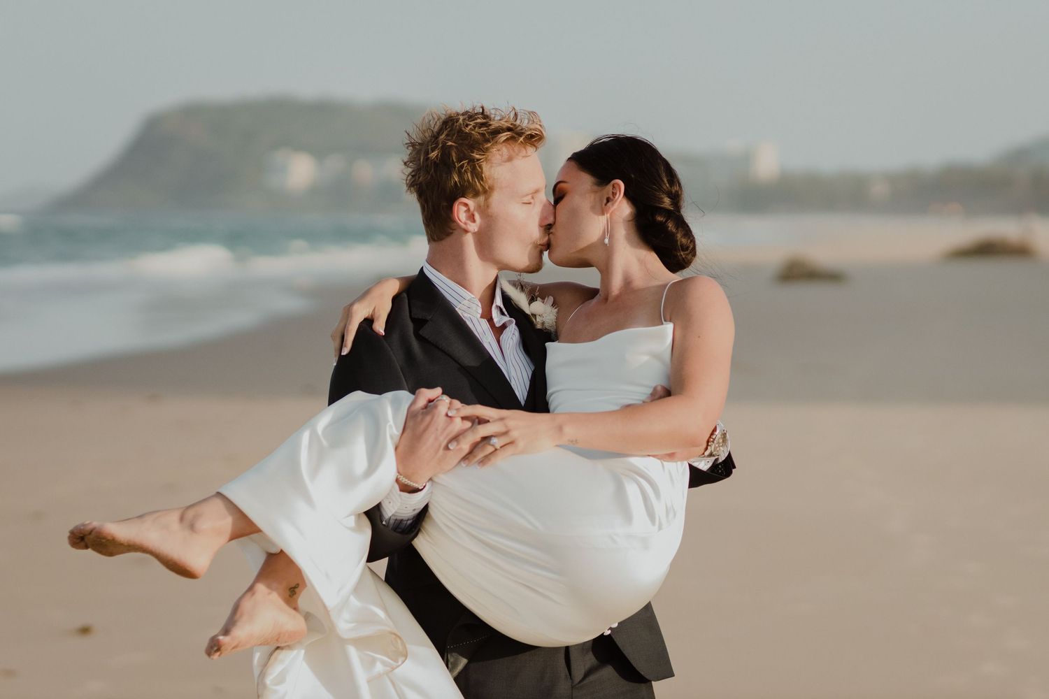 Romantic beach wedding photos with couple dancing and embracing on sandy shore.