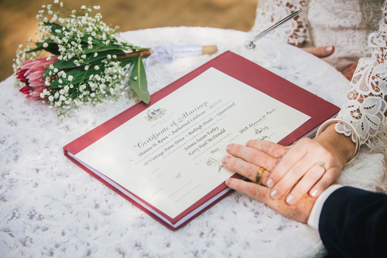 Close-up of hands resting on wedding document with lace dress detail and flowers in frame.DIY wedding Gold Coast elopement photographer Gold