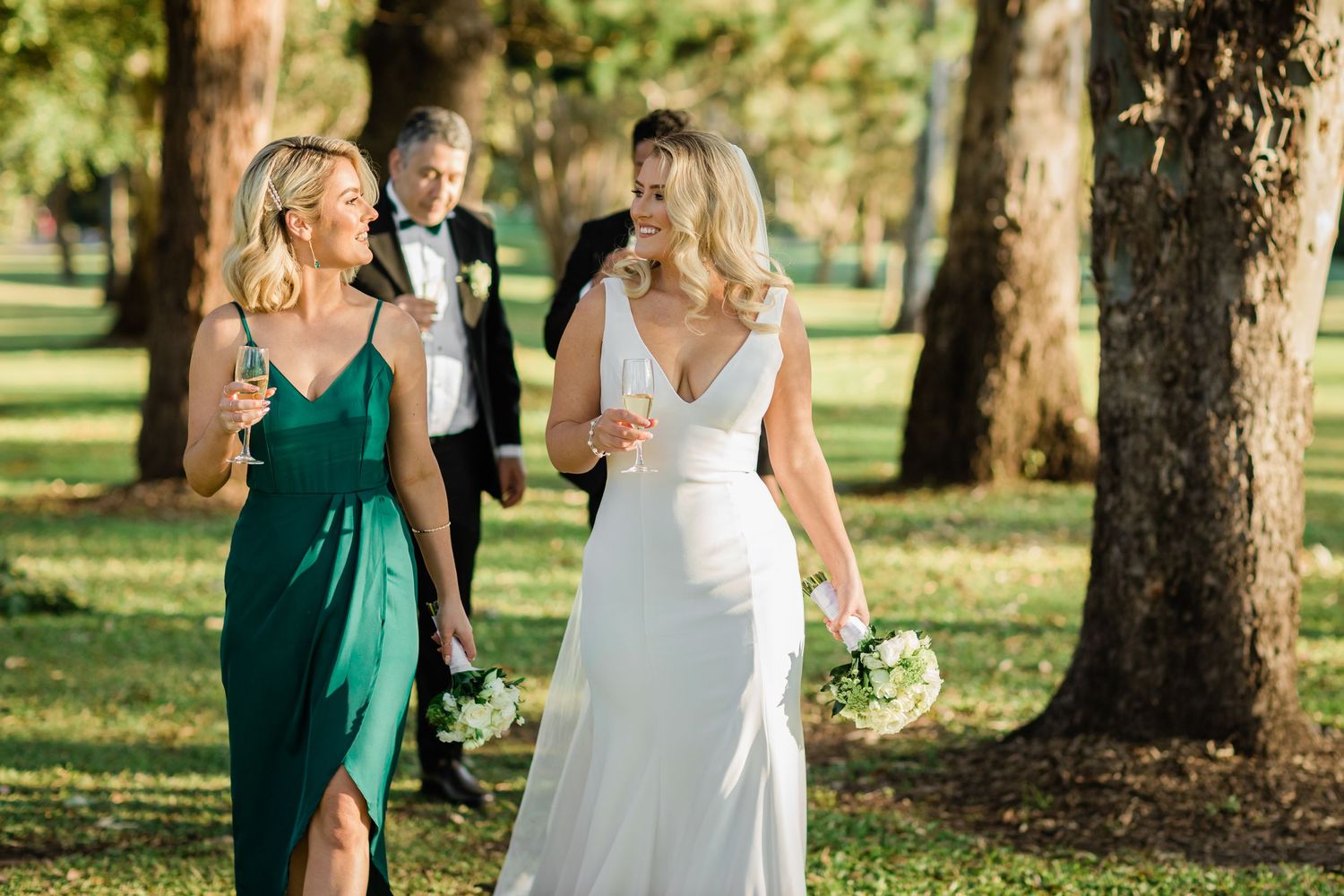 A wedding party walks through a sunlit forest with bridesmaids in emerald green dresses and white bouquets. Surfers Paradise Golf Club weddi