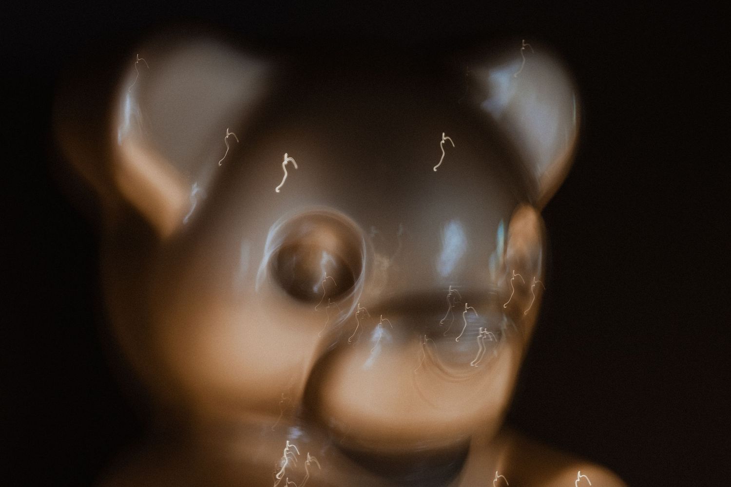Close-up artistic shot of a blurred teddy bear figurine against dark background.