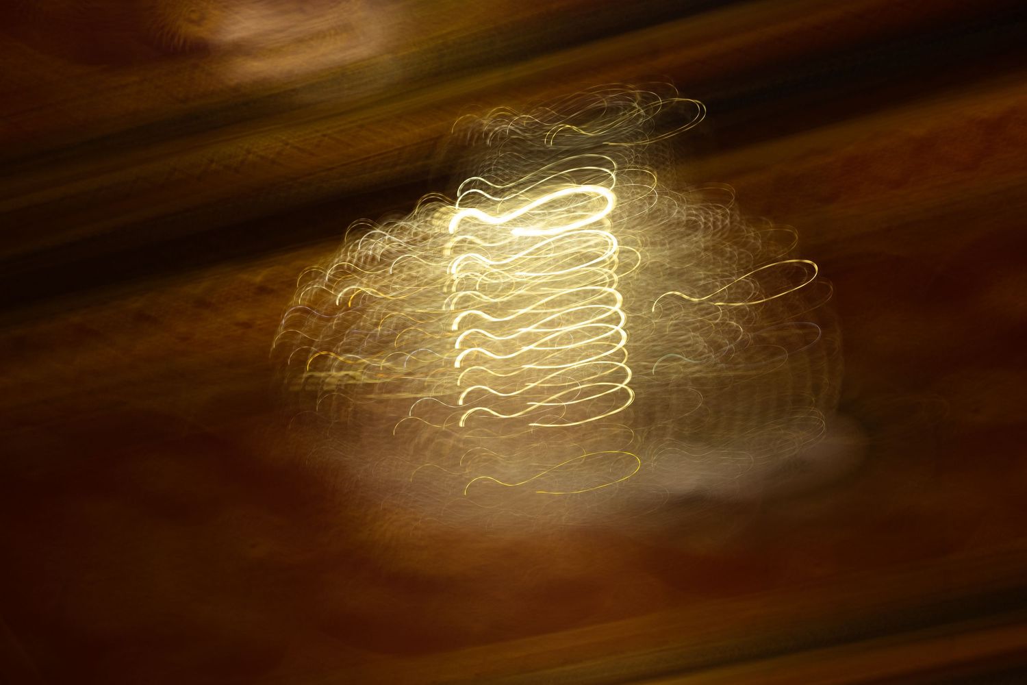Light painting photography showing golden streaks against dark brown background.
