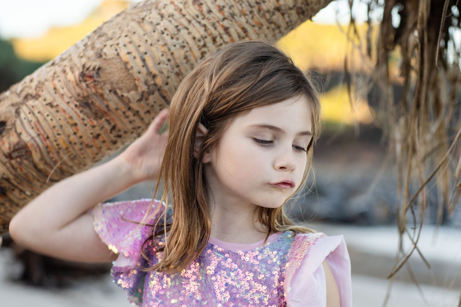 Young person in a floral dress posing thoughtfully near a tree trunk.Family photography cabarita New South Wales Cabarita headland