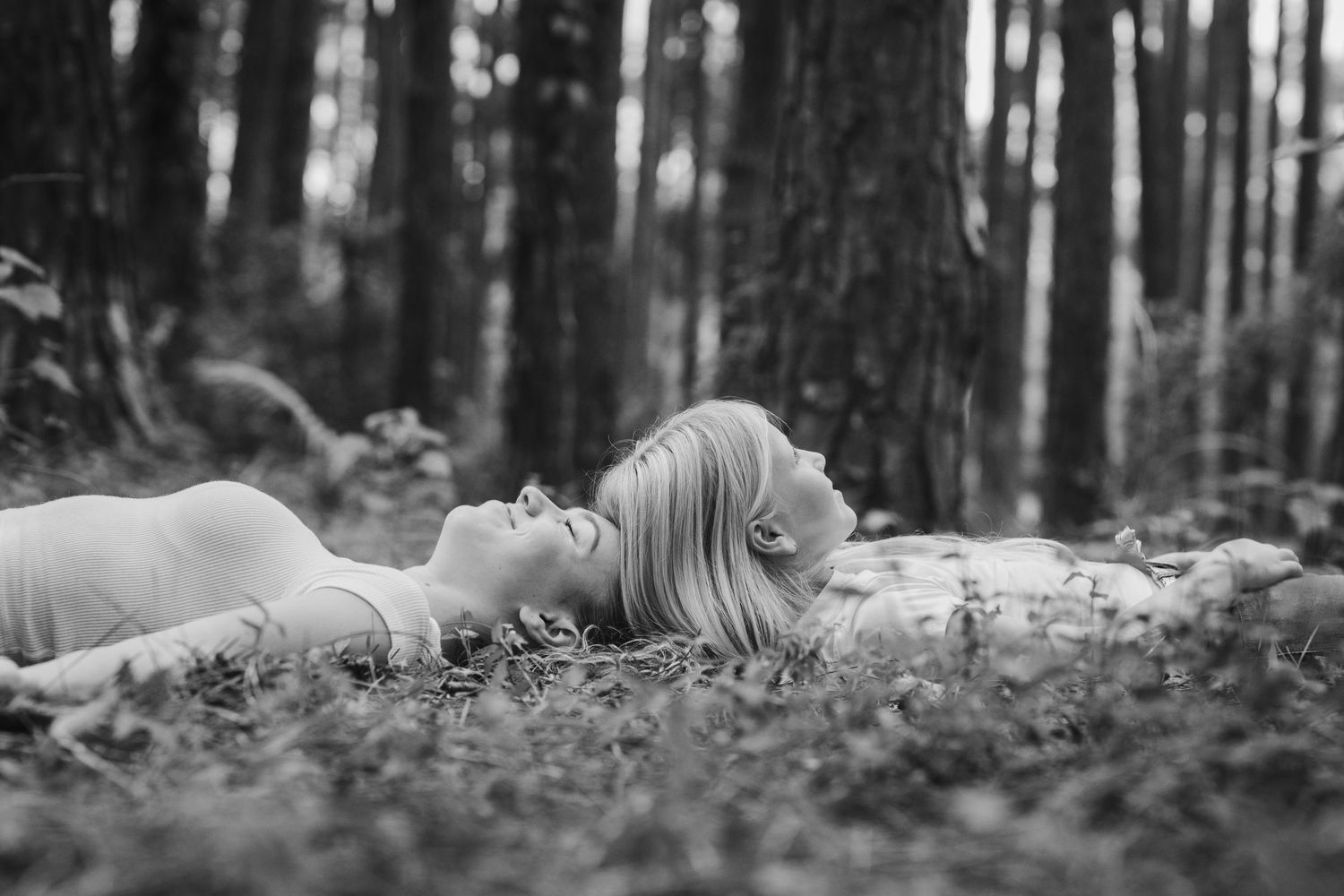 Artistic black and white photography of people lying on forest floor surrounded by pine needles.Pizzey park family photos. Gold Coast