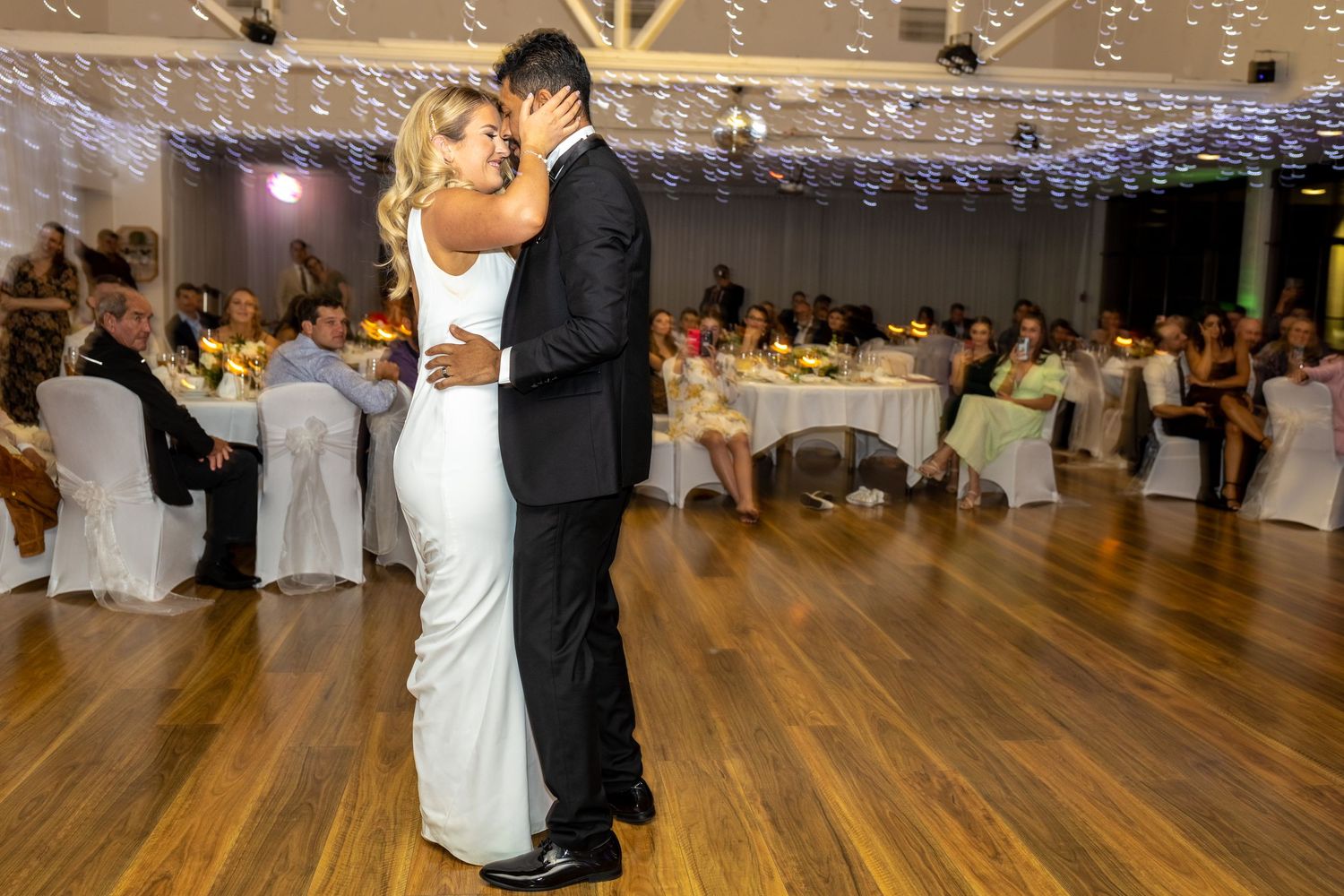 Couples dancing on wooden floor during evening wedding reception.