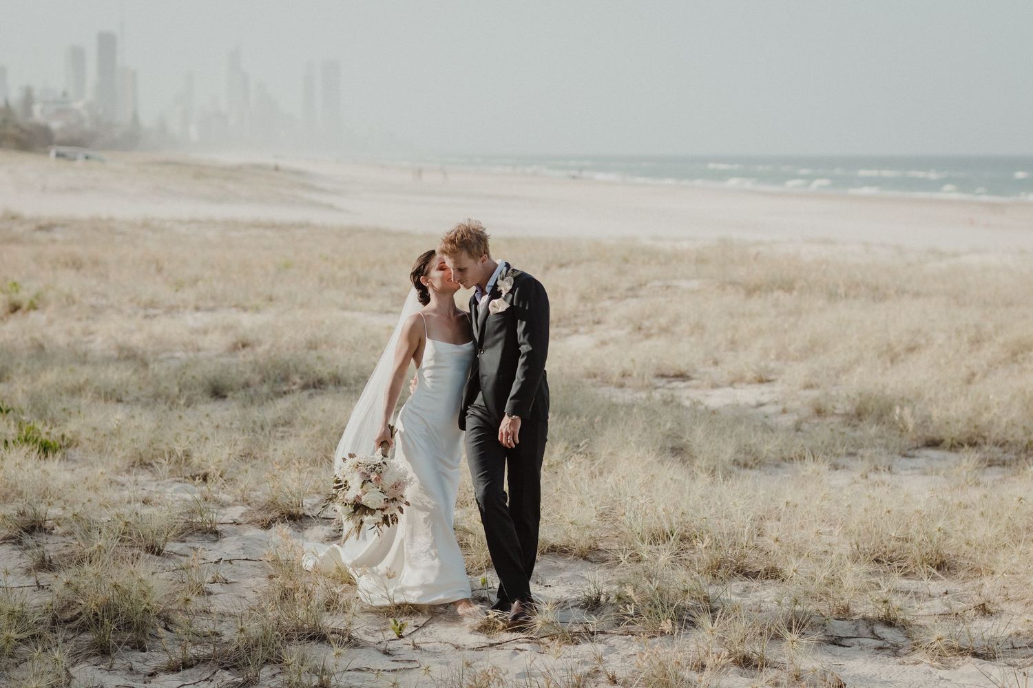 Romantic coastal wedding portraits with city skyline visible in the background.