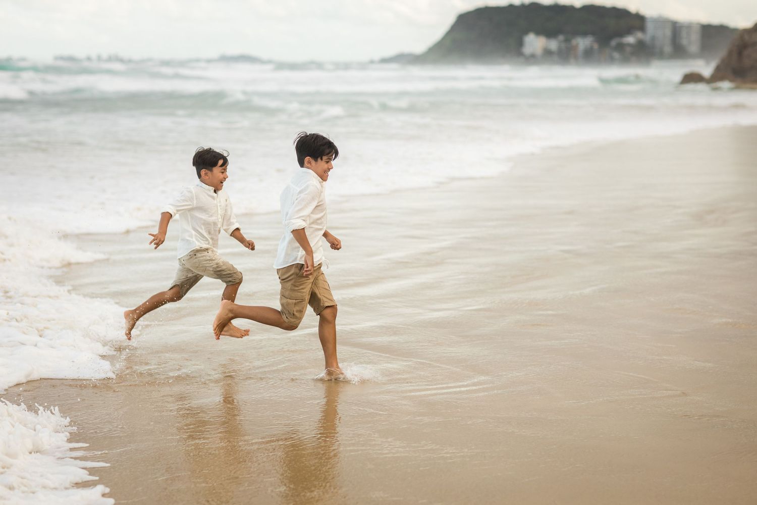 Children playing and running along a sandy beach with cliffs in the background.Gold Coast candid family photographer.