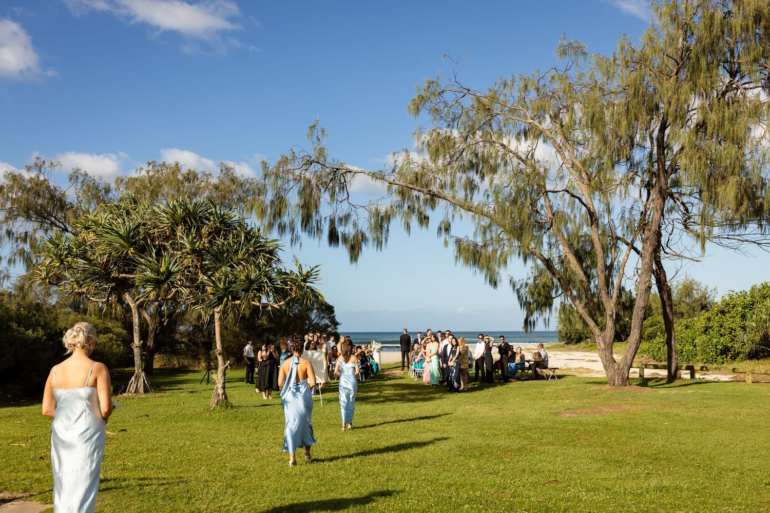 Panoramic view of outdoor wedding ceremony under trees with ocean backdrop.