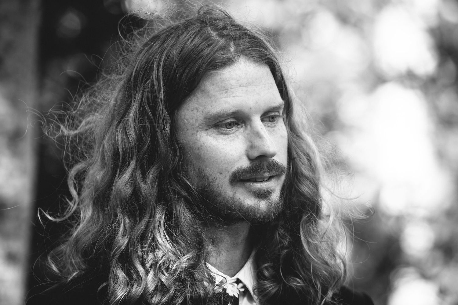 Black and white portrait of a person with long wavy hair and a beard smiling softly at the camera.DIY wedding Gold Coast elopement photograp