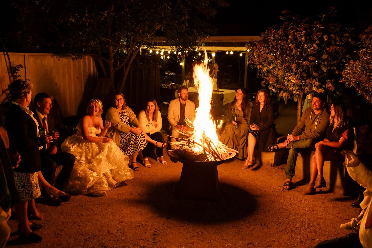Nighttime wedding reception with bonfire and guests gathered under string lights.Tallebudgera family photography. Gold Coast