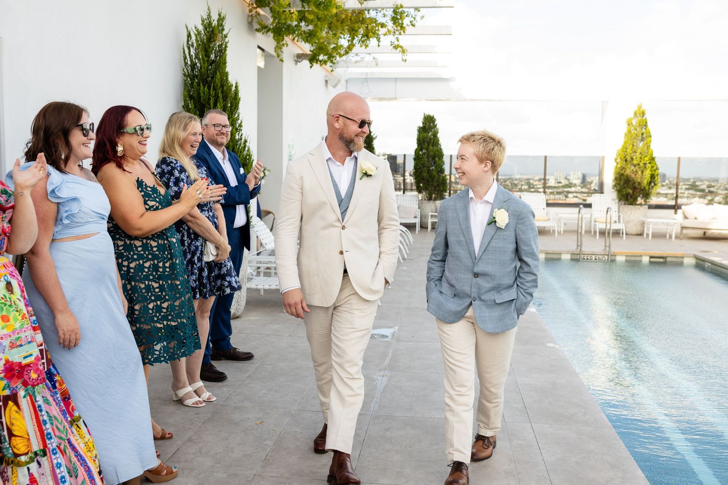 Wedding guests gather on an elegant rooftop venue with white decor and city views in the background.