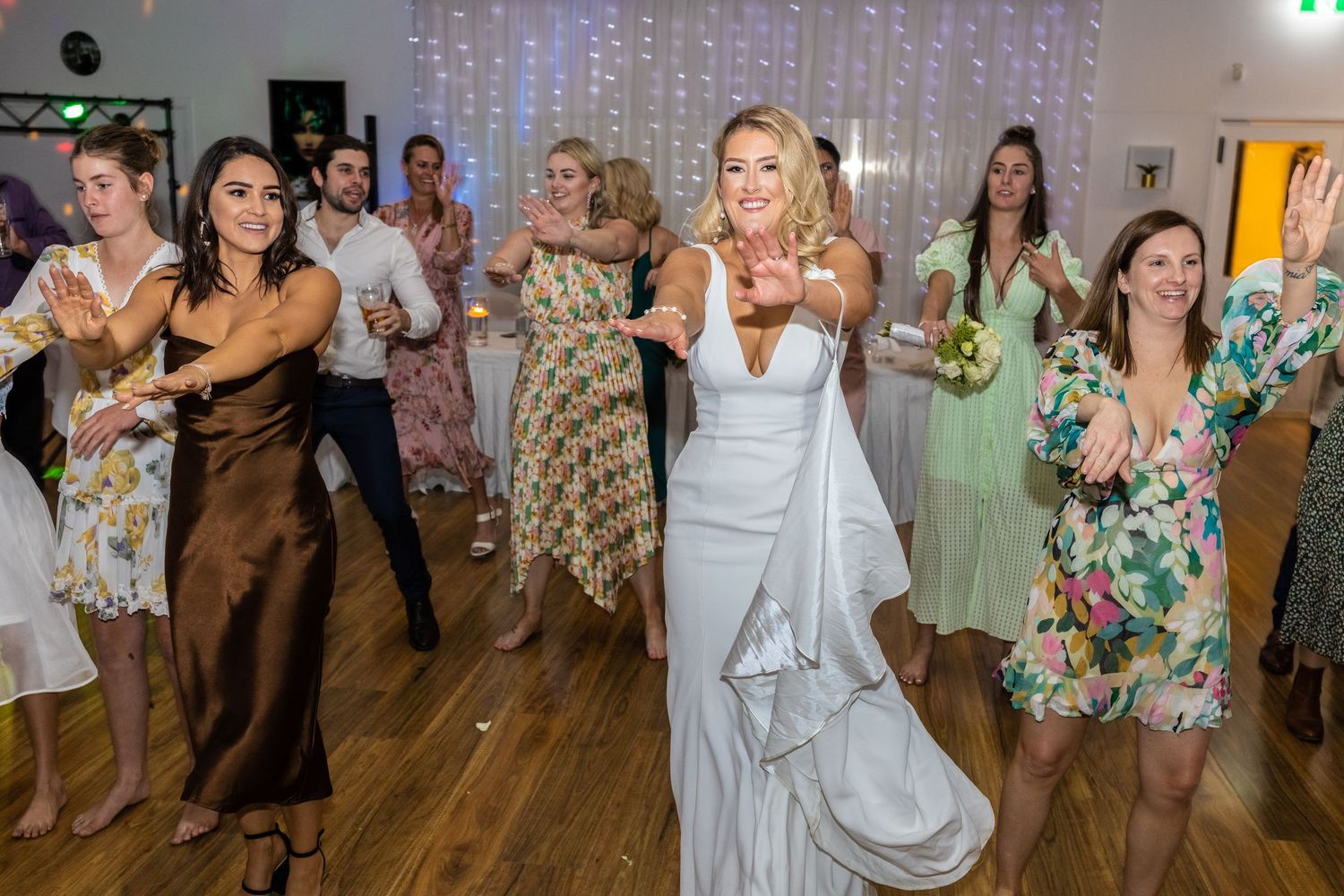 Wedding celebration with guests dancing in formal attire on wooden dance floor.