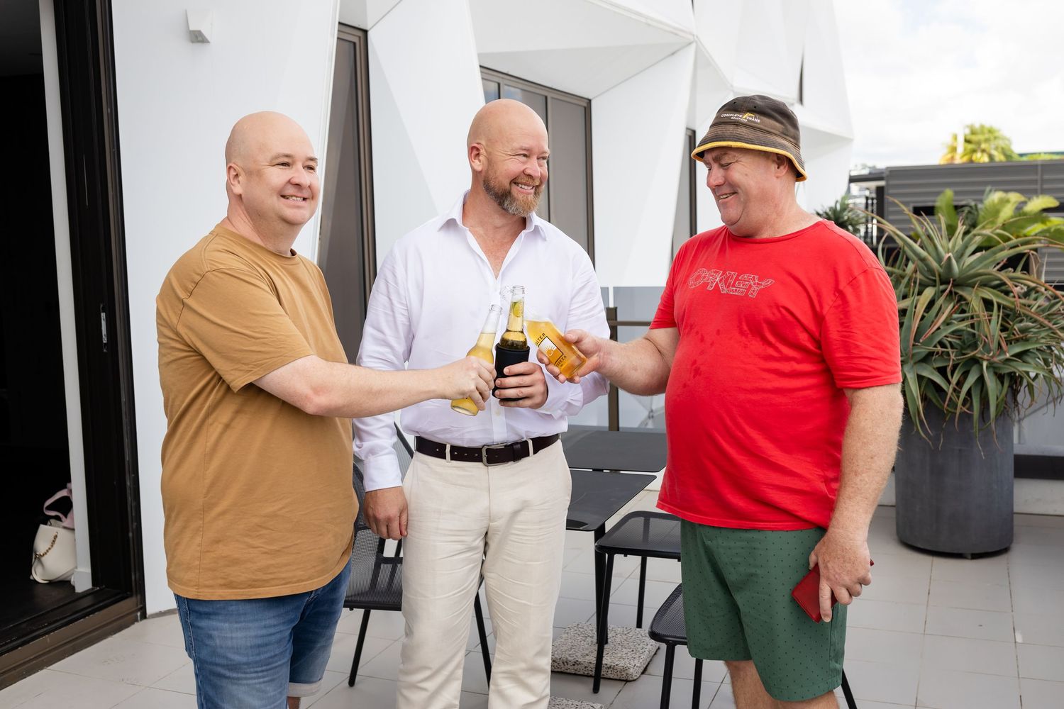A group enjoying drinks and conversation on an outdoor patio with white walls and planters.